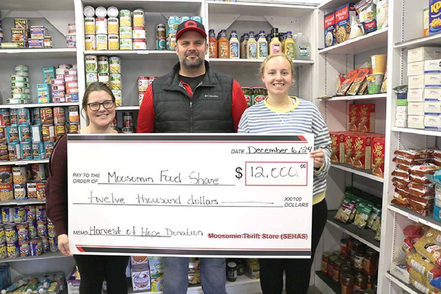 Kyle Penner with Harvest of Hope making a $12,000 donation to the Moosomin Food Share with proceeds from the 2024 harvest. At left is Samantha Campbell with the Food Share and at right is Jaedyn Moore with the Food Share.